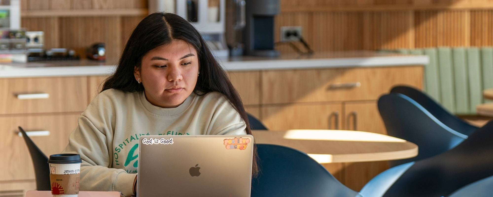 Student sitting at a table working on a laptop in the Thompson Student Success Center.